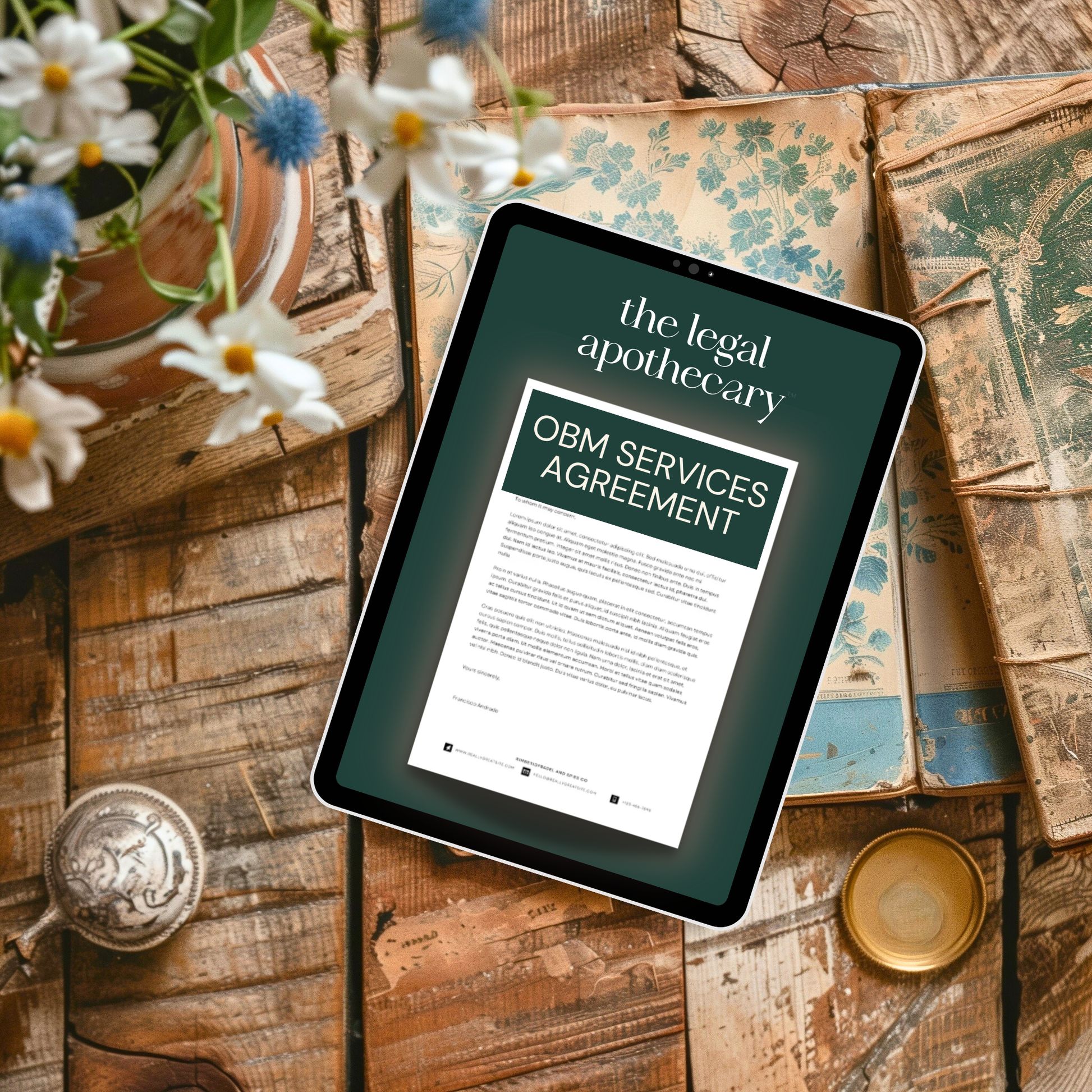 Tablet displaying 'the legal apothecary' document an an O.B.M. services agreement mockup on a wooden surface with flowers and books.